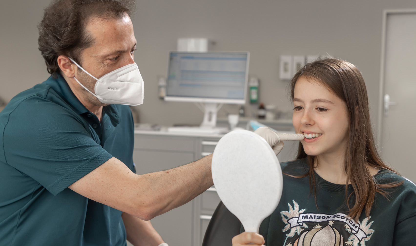 Kieferorthopäde bespricht die Behandlung mit einer Jugendlichen und zeigt auf Ihre Zähne.