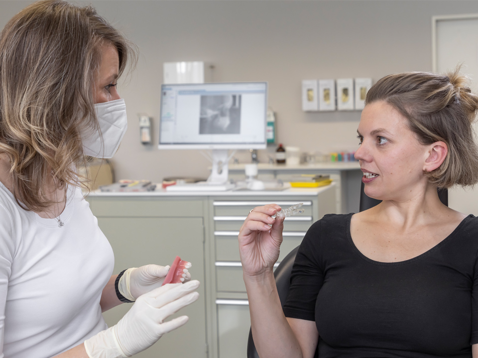 Patientin mit Kieferorthopädin im Gespräch, Ärztin hält Zahnmodell in den Händen.